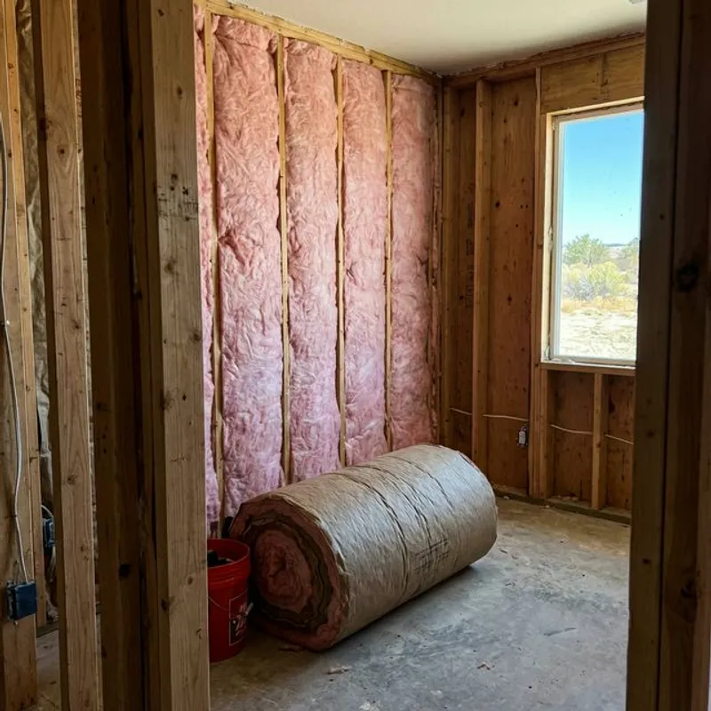 Pink fiberglass batt insulation installed between wall studs in residential room