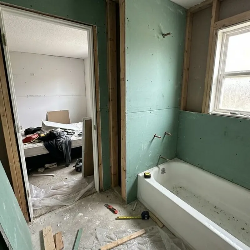 Green-faced mold-resistant drywall being installed in residential bathroom around bathtub and shower area